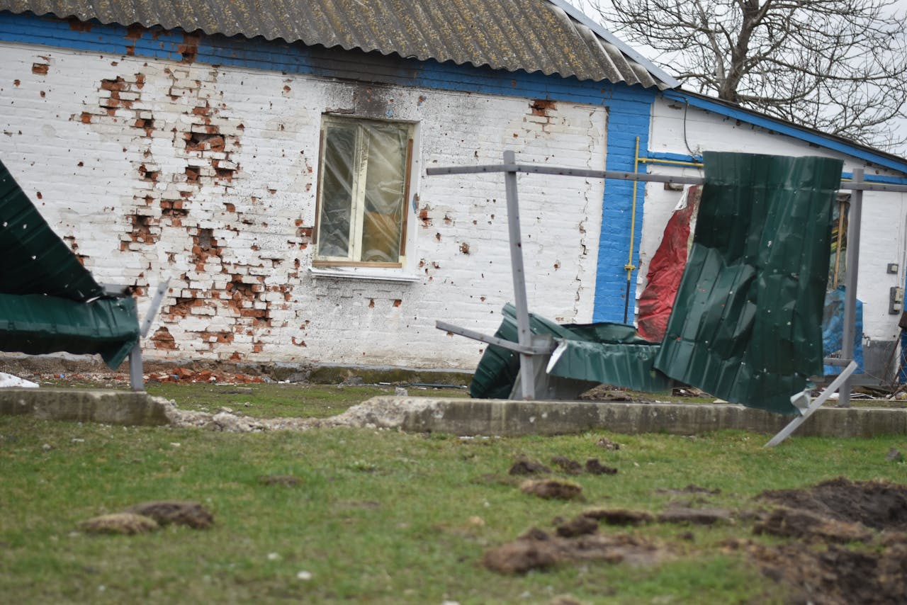 Rural house with damaged brick wall and broken fence, depicting decay and neglect.