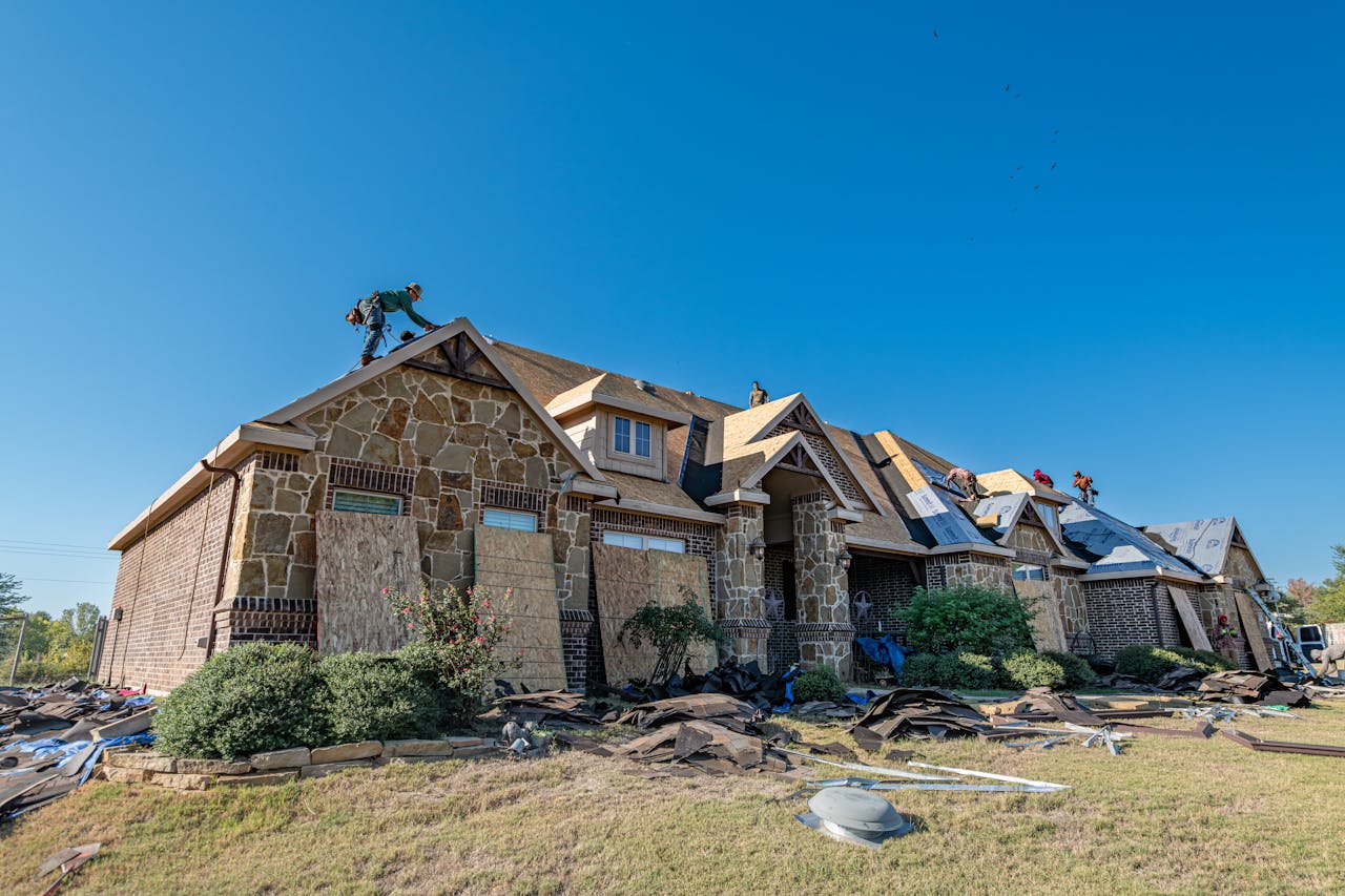 Brick house in Weatherford, Texas undergoing roof installation. Workers on roof under clear sky.